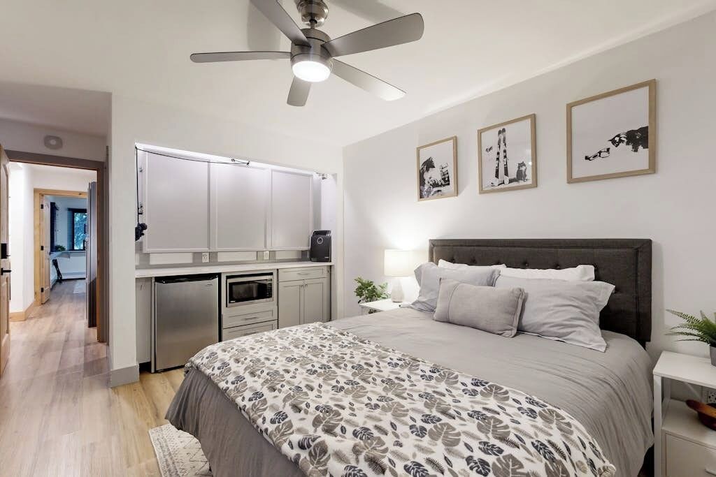 Ein Schlafzimmer mit einem Bett, Nachttisch, Lampe, Deckenventilator und einem Kunstwerk an der Wand.