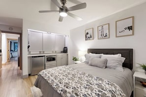 Ein Schlafzimmer mit einem Bett, Nachttisch, Lampe, Deckenventilator und einem Kunstwerk an der Wand.