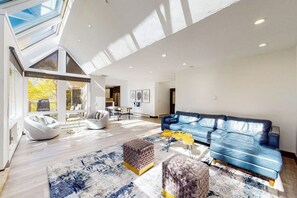 A spacious living room with a blue leather sofa, a white bean bag chair, and a patterned rug. - Three-story townhouse with balcony, mountain views, fireplace, grill, & W/D (Vail)