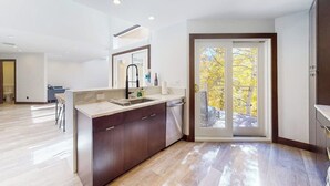 A modern kitchen with a central island, a dining area, and a sliding glass door leading to a balcony. - Three-story townhouse with balcony, mountain views, fireplace, grill, & W/D (Vail)