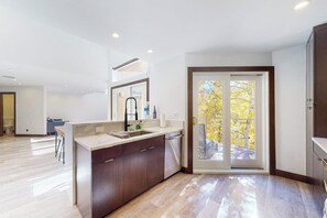 A modern kitchen with a central island, a dining area, and a sliding glass door leading to a balcony. - Three-story townhouse with balcony, mountain views, fireplace, grill, & W/D (Vail)