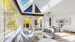 A modern interior with a large window, two seating areas, a dining table, and artwork on the wall. - Three-story townhouse with balcony, mountain views, fireplace, grill, & W/D (Vail)