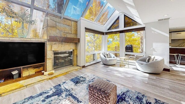 A modern living room with a fireplace, large windows, and a flat-screen TV. - Three-story townhouse with balcony, mountain views, fireplace, grill, & W/D (Vail)