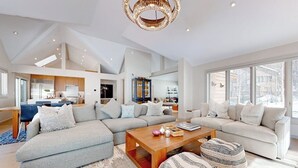 Een ruime woonkamer met een grote modulaire bank, een houten salontafel en een kroonluchter.