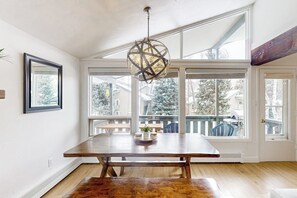 A dining area with a wooden table, a hanging light fixture, and large windows with a view of a snowy landscape. - Cozy Condo walk to Lionshead, On Bus Route (Vail)