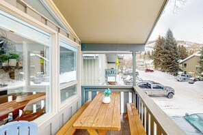 A covered outdoor seating area with a wooden table and benches, overlooking a snowy street with parked cars and buildings. - Cozy Condo walk to Lionshead, On Bus Route (Vail)