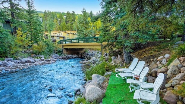 Un río con rocas, un puente y una fila de sillas blancas sobre una alfombra verde.
