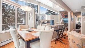 Una cocina moderna con una isla grande, un área de comedor con mesa y sillas de madera, y vistas al exterior a través de amplios ventanales.