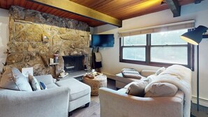 A cozy living room with a stone fireplace, a flat-screen TV, and a large window. - Remodeled, mountain view townhome with patio, fireplace & great location (Vail)