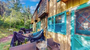 A wooden cabin with a covered outdoor seating area, a large window, and a door with a cross design. - Remodeled, mountain view townhome with patio, fireplace & great location (Vail)