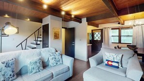 A living room with a staircase, a dining area, and a view of the outdoors. - Remodeled, mountain view townhome with patio, fireplace & great location (Vail)