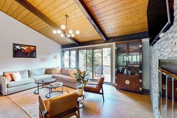 A spacious living room with a wooden ceiling, a sofa set, a coffee table, and a fireplace.