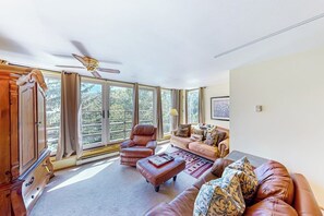 A spacious living room with a large window, leather furniture, and a ceiling fan. - Rustic condo with resort amenities, sweeping views, and wood-burning fireplace (Vail)