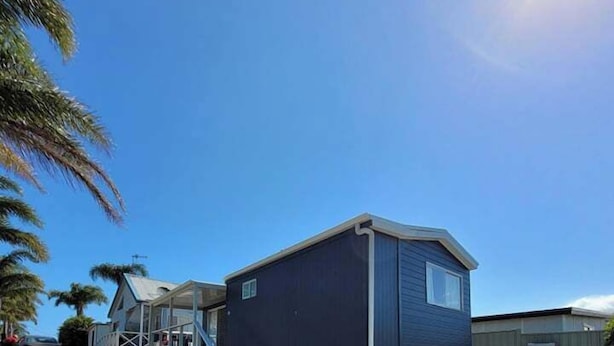 Une maison mobile de plain-pied, dotée d’un porche couvert et d’une allée en béton.