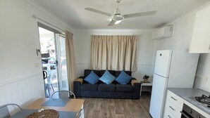 A compact living space with a kitchenette, a dining area, and a seating area with a sofa. - Morton A - Cabin with Views and Deck (Mollymook)