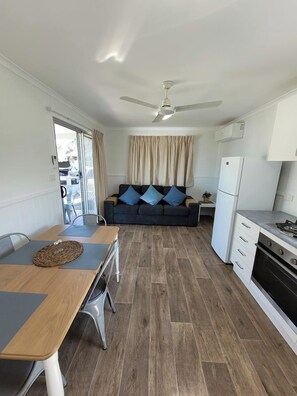 Een ruimtelijk ingerichte leefruimte met een kitchenette, een eethoek en een zithoek met een bank.