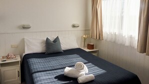 Ett hotellrum med en säng, ett nattduksbord, en lampa, ett fönster med gardiner och en väggmonterad lampa.