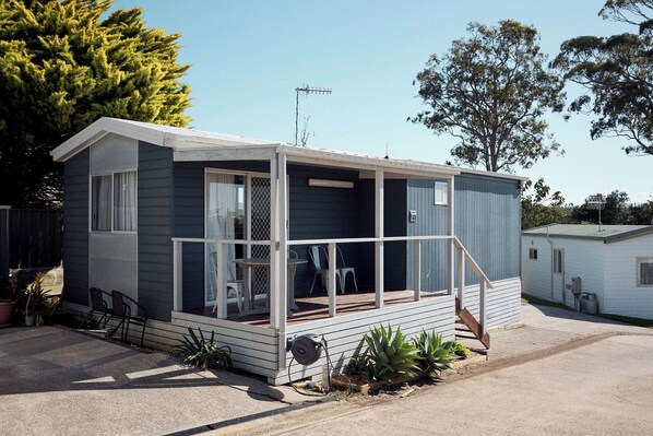A small, single-story mobile home with a porch, a sliding door, and a small deck area.
