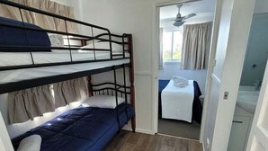 Une chambre avec un lit superposé, une petite table avec une serviette, et une salle de bain visible à travers une porte ouverte.