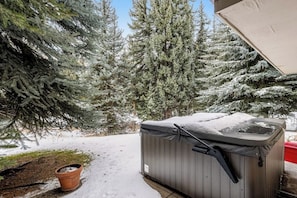 Ein Whirlpool im Freien, bedeckt mit Schnee, umgeben von Bäumen.