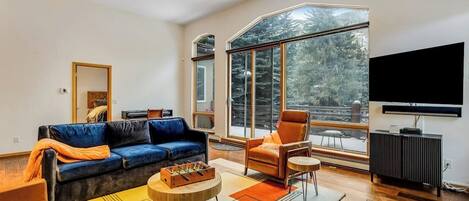 A modern living room with a blue sofa, an orange armchair, a coffee table, and a large window with a view of trees.