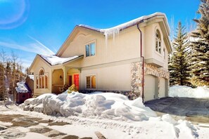 A two-story house with a stone facade, a garage, and snow accumulation around the property. - Secluded 3-story home with mountain views, fireplace, washer/dryer, & jetted tub (Vail)