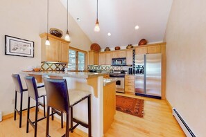A kitchen with wooden cabinets, stainless steel appliances, a bar area with stools, and pendant lighting. - Secluded 3-story home with mountain views, fireplace, washer/dryer, & jetted tub (Vail)