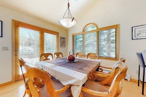 A dining room with a table set for six, wooden chairs, a chandelier, and large windows with blinds. - Secluded 3-story home with mountain views, fireplace, washer/dryer, & jetted tub (Vail)