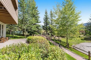 A building with a wooden exterior, a paved patio with benches, and a pathway leading to a parking area. - Sunlit, mountain view condo with a fireplace plus on-site pool & hot tub (Vail)