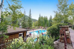A wooden cabin with a pool, surrounded by trees and a mountain backdrop. - Sunlit, mountain view condo with a fireplace plus on-site pool & hot tub (Vail)