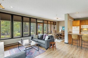 A spacious living area with a sofa, coffee table, and a view through large windows. - Sunlit, mountain view condo with a fireplace plus on-site pool & hot tub (Vail)
