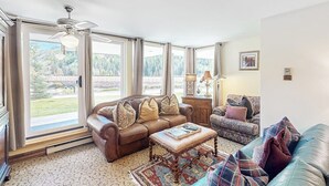 A spacious living room with a large window, a ceiling fan, and a fireplace. - Charming condo with resort amenities, sweeping views, & wood-burning fireplace (Vail)