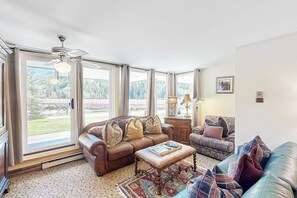 A spacious living room with a large window, a ceiling fan, and a fireplace. - Charming condo with resort amenities, sweeping views, & wood-burning fireplace (Vail)
