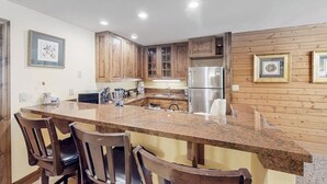 A kitchen with wooden cabinets, a granite countertop, and a stainless steel refrigerator. - Charming condo with resort amenities, sweeping views, & wood-burning fireplace (Vail)