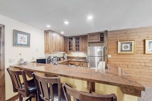 A kitchen with wooden cabinets, a granite countertop, and a stainless steel refrigerator. - Charming condo with resort amenities, sweeping views, & wood-burning fireplace (Vail)