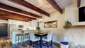 Una cocina moderna con armarios blancos, una isla central y una zona de comedor con una mesa de madera oscura y sillas de color claro.
