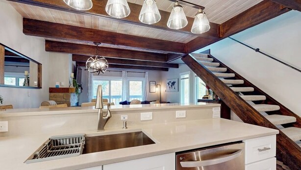 Una cocina con un lavamanos de acero inoxidable, muebles blancos y una escalera de madera.