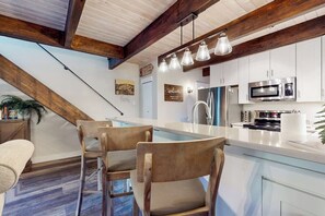 Eine moderne Küche mit weißen Schränken, einer Edelstahl-Mikrowelle und einem eingebauten Backofen. Es gibt einen Essbereich mit Holztisch und Stühlen sowie eine hängende Leuchte.
