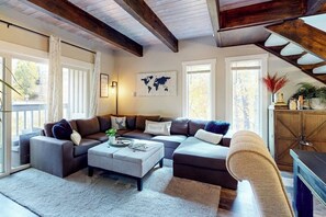 Ein Wohnzimmer mit einer Eckcouch, einem Couchtisch und einer Katzenkralle. Es gibt große Fenster und eine Weltkarte an der Wand.