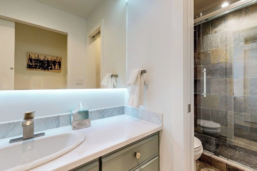 A bathroom with a marble countertop, a sink, a mirror, and a glass-enclosed shower.