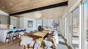 A modern kitchen with wooden cabinets, a central island with stools, and a large dining table with white furry chairs. - Luxury, designer mountain perch with amazing views, chef's kitchen & hot tub (Vail)