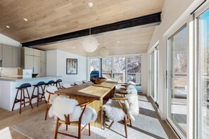A modern kitchen with wooden cabinets, a central island with stools, and a large dining table with white furry chairs. - Luxury, designer mountain perch with amazing views, chef's kitchen & hot tub (Vail)