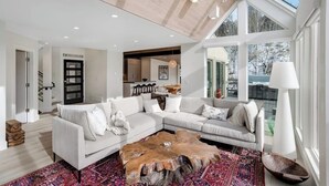 A spacious living room with a large sectional sofa, a wooden coffee table, and a view of the outdoors through large windows. - Luxury, designer mountain perch with amazing views, chef's kitchen & hot tub (Vail)