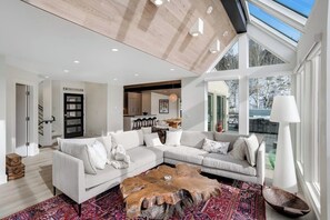A spacious living room with a large sectional sofa, a wooden coffee table, and a view of the outdoors through large windows. - Luxury, designer mountain perch with amazing views, chef's kitchen & hot tub (Vail)