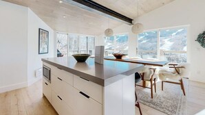 A modern kitchen with a large island, wooden flooring, and large windows offering a mountain view. - Luxury, designer mountain perch with amazing views, chef's kitchen & hot tub (Vail)