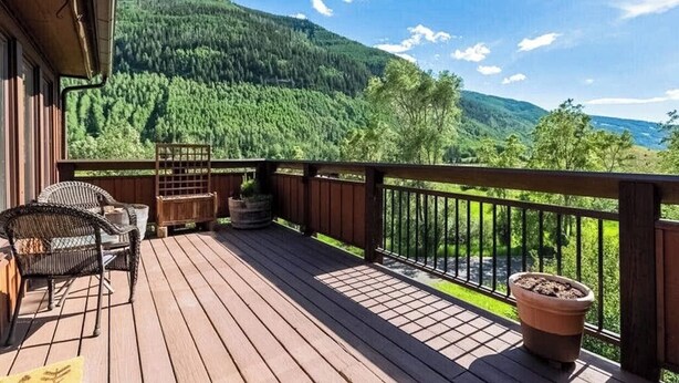 Une terrasse en bois, dotée de mobilier d’extérieur, d’une rambarde et offrant une vue sur une montagne boisée.
