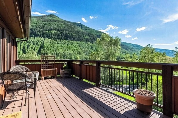 Eine Holzterrasse mit Gartenmöbeln, einem Geländer und Blick auf einen bewaldeten Berg.