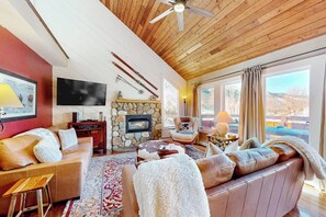 Ein gemütliches Wohnzimmer mit Kamin aus Stein, Ledersofas, einem Flachbildfernseher und einem großen Fenster mit Vorhängen.