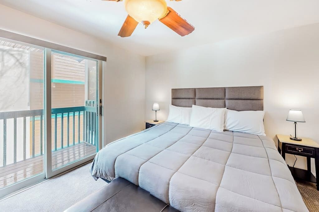 A bedroom with a bed, nightstands, a ceiling fan, and a sliding glass door to a balcony.