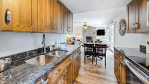 A kitchen with wooden cabinets, granite countertops, a built-in stove, and a dining area with a table and chairs. - Mountain view condo with 2 balconies, pool & pickleball - steps to free shuttle (Vail)